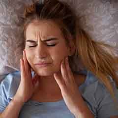 Woman rubbing her aching jaw in bed