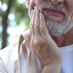 Man rubbing his jaw with blurred trees in background