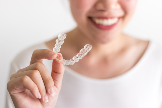 young woman holding Invisalign clear aligner